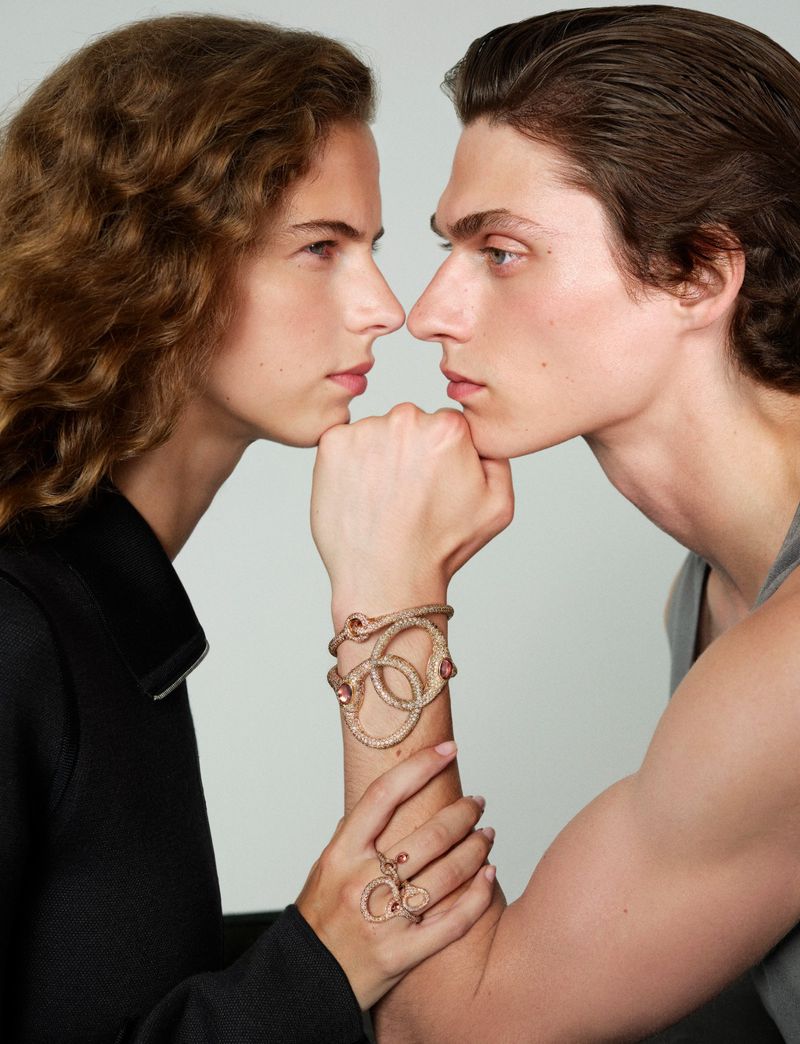 Two models facing each other with hands clasped together displaying intricate serpentine jewelry for Numero China.