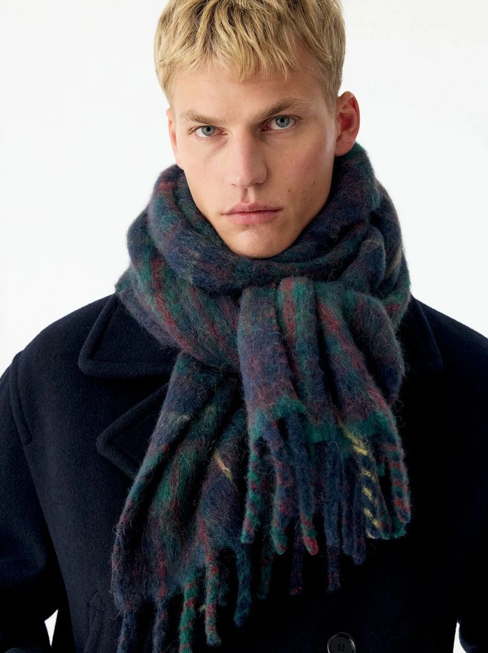 Model Timo Pan wearing a chunky plaid scarf and dark coat against a plain white background for Arket knitwear project by Andreas Öhlund
