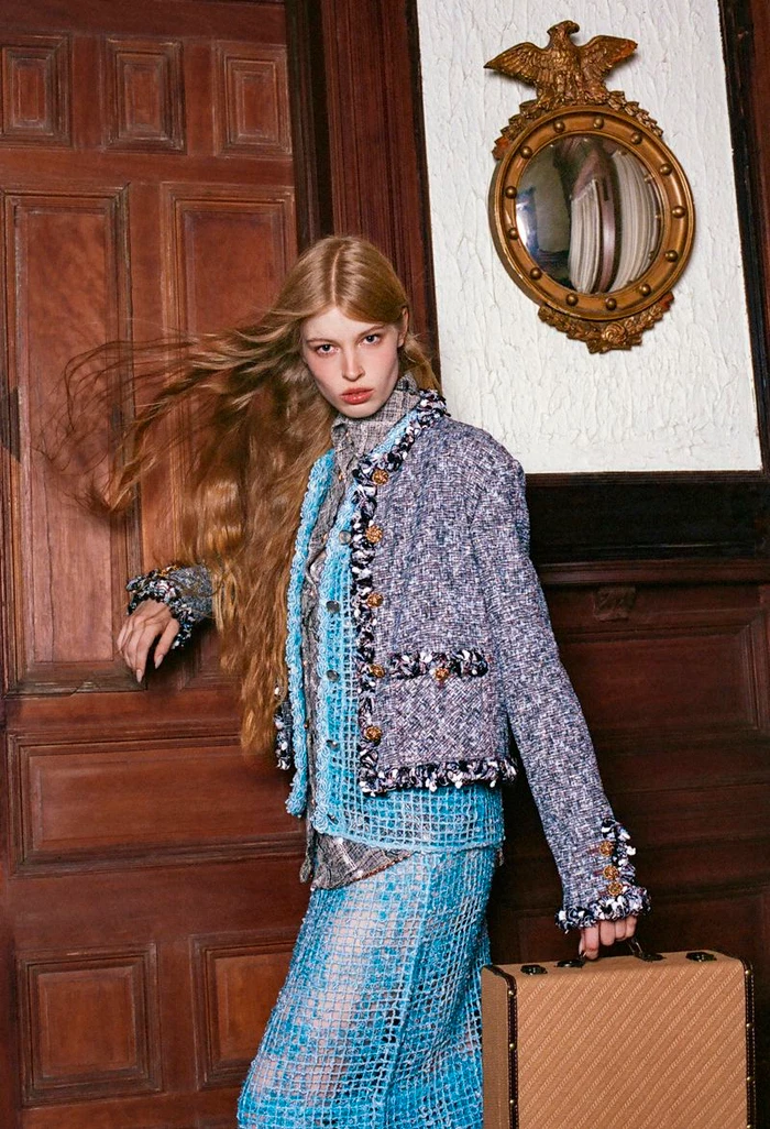 Model with long blonde hair holding a small suitcase in front of wood paneling and a round mirror for Vogue Czechoslovakia