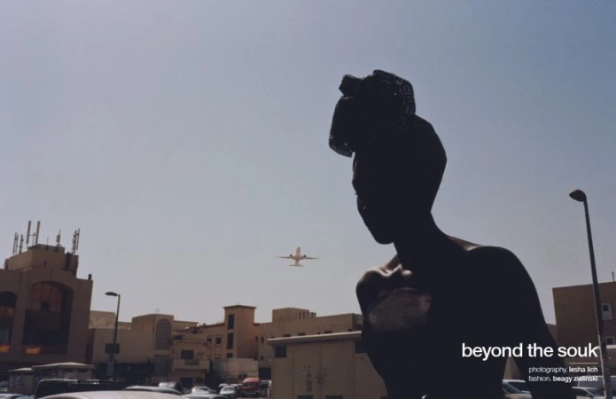 Silhouette of an adult wearing a headwrap in front of city buildings with an airplane visible in the sky on a sunny day.