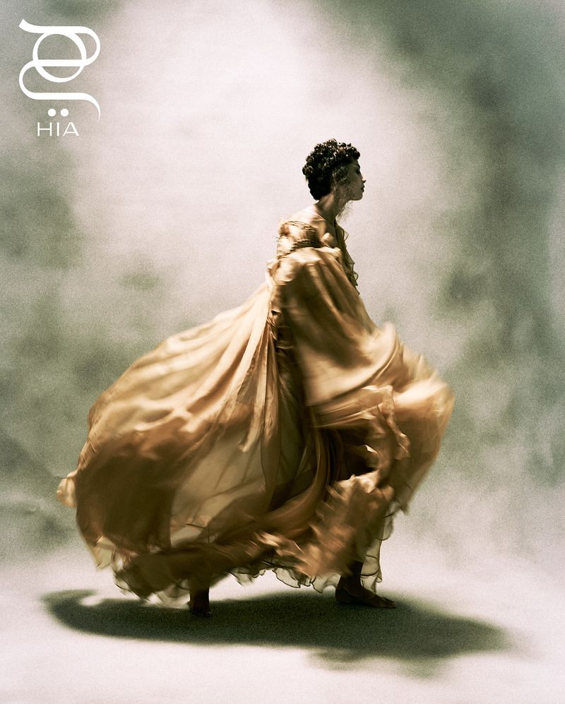 Woman in flowing gold gown poses in studio with dramatic lighting and smoky background for fashion or artistic portraiture.