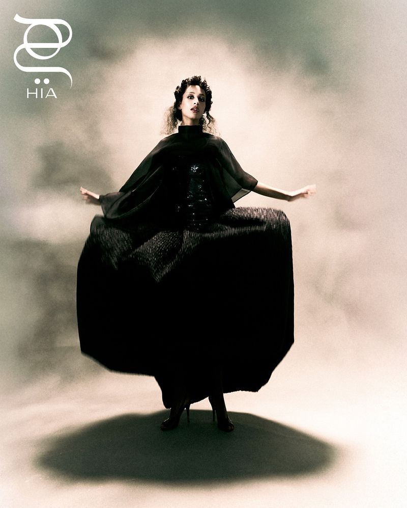 A striking fashion image of an adult female model in a dark, flowing gown with smokey background. Dramatic full-body shot with elegant pose.