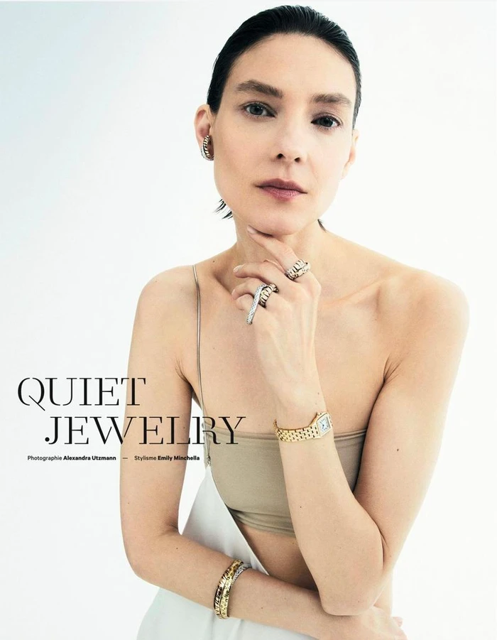 Model wearing gold watch and luxury rings with hand resting under chin against white backdrop