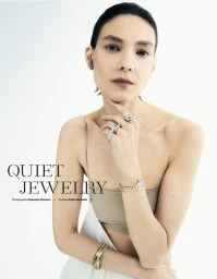 Model wearing gold watch and luxury rings with hand resting under chin against white backdrop