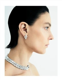 Profile portrait of a woman wearing a geometric diamond earring and a segmented silver necklace against a plain white background.