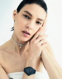 Close-up portrait of model Kati Nescher wearing a crystal choker and dark watch against a white background