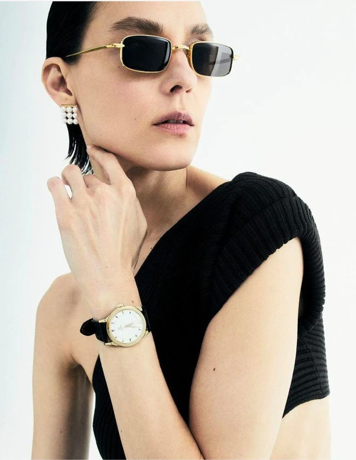 Model wearing dark sunglasses, gold earrings, and a wristwatch against a white background for Les Echos Joaillerie.