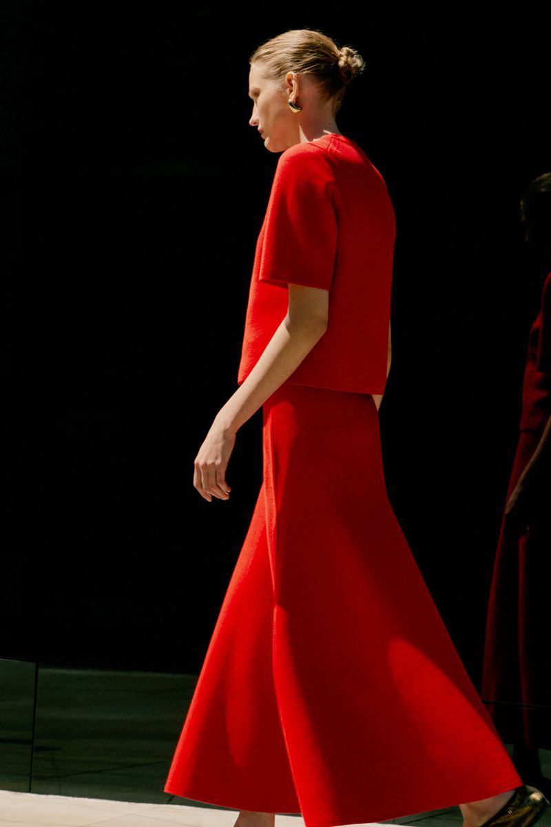Fashion model showcases a modern, elegant red ensemble with a high neckline, paired with wide-leg trousers against a dark backdrop.