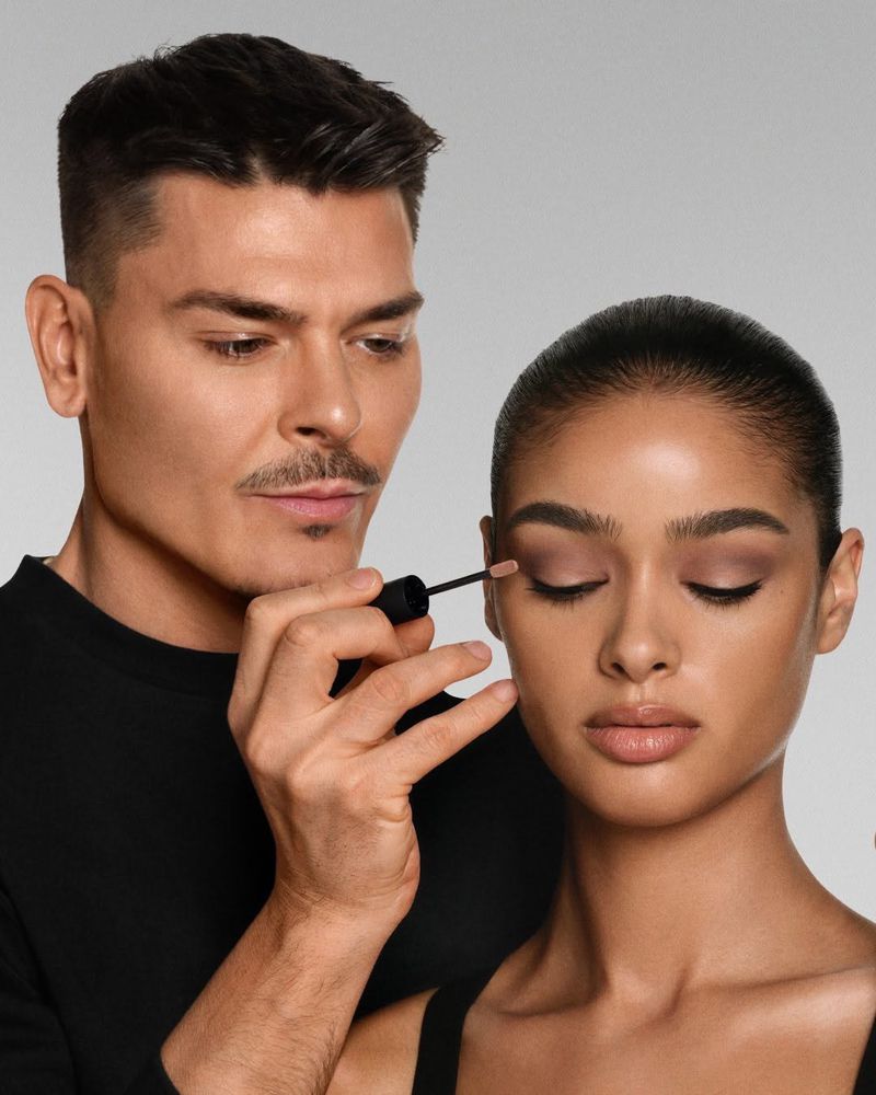 Makeup artist applying eyeshadow to a model in a studio setting, showcasing beauty and cosmetic application with focus on eye makeup.