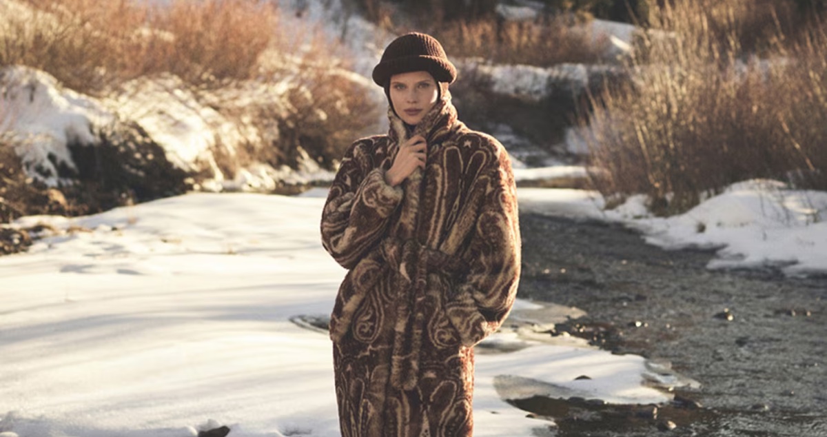 Model Ida Heiner wearing a patterned brown coat and beanie in a snowy landscape for Loro Piana