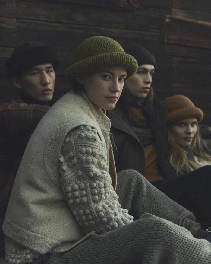 Four models wearing knitwear and winter hats pose against a rustic dark wooden wall for Loro Piana Holiday 2026.