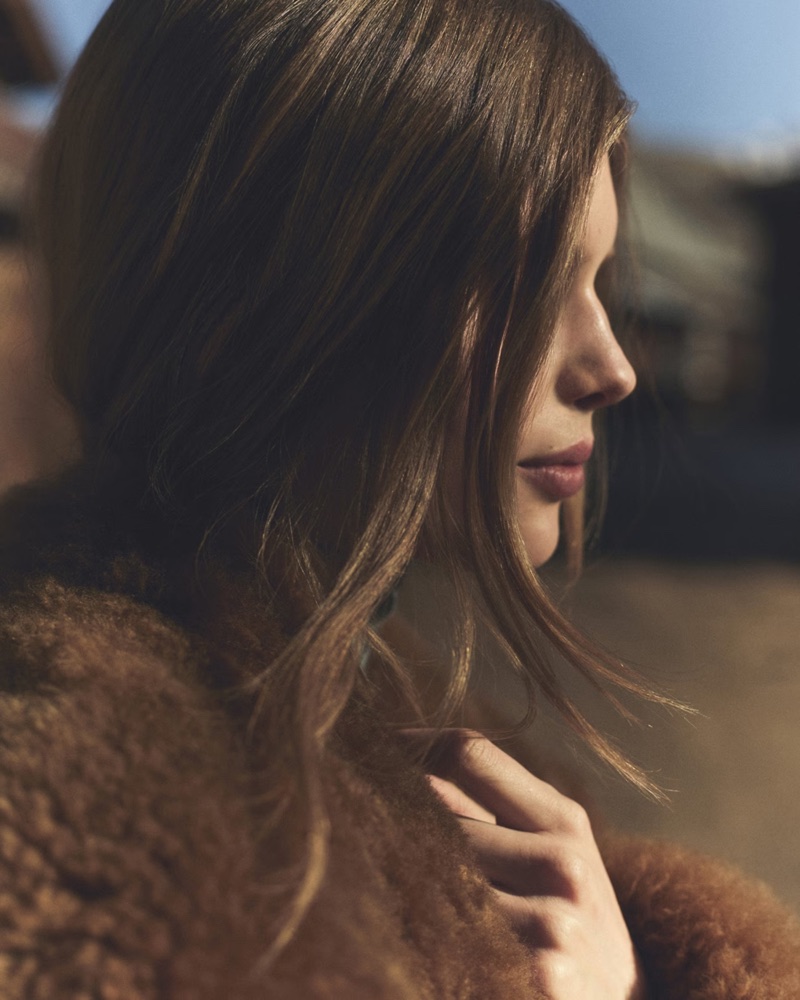 Close-up profile of a woman wearing a plush brown shearling coat with soft natural daylight.
