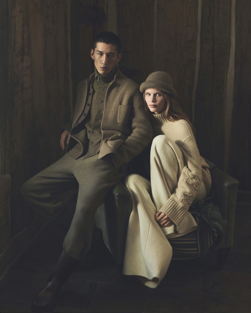 Two models wearing knitwear and wool trousers seated in a dark wood-paneled interior for Loro Piana Holiday 2026