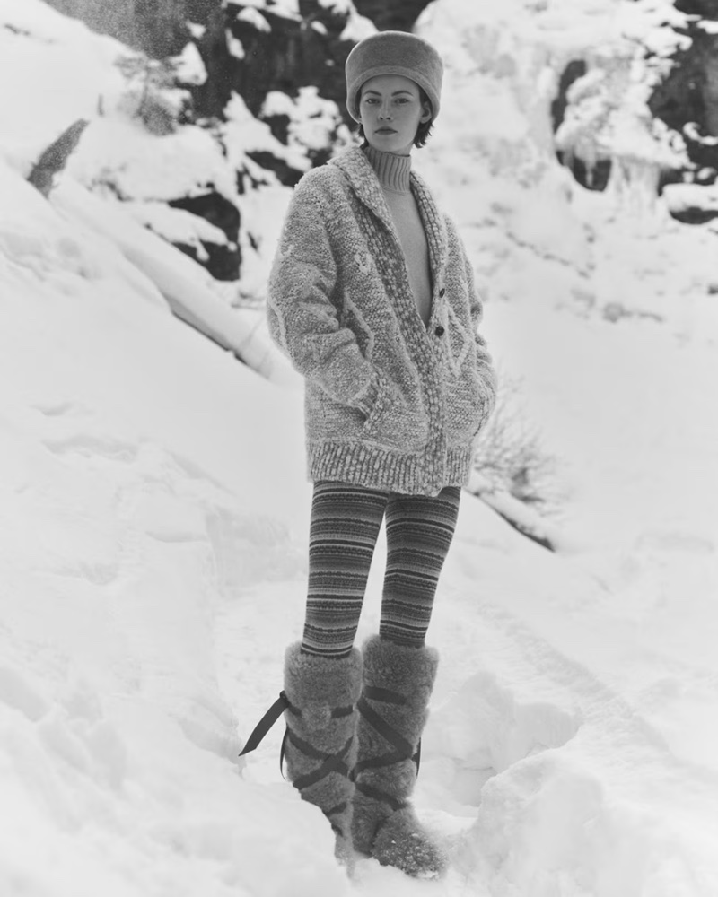Model wearing a chunky knit cardigan, patterned leggings, and tall fur boots standing outdoors in snow