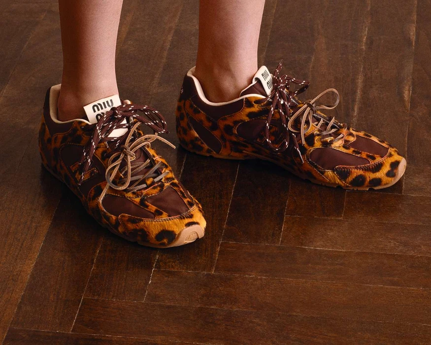 Close-up of leopard print sneakers with brown laces and visible branding standing on a dark wooden parquet floor.