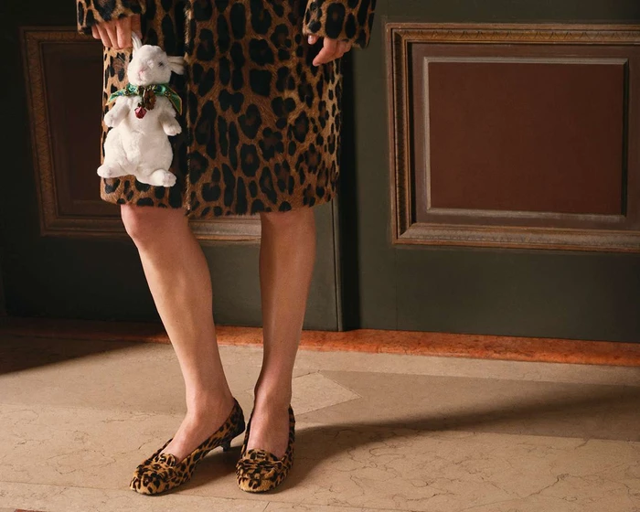 Model wearing leopard print coat and matching kitten heels holding a small white stuffed rabbit prop