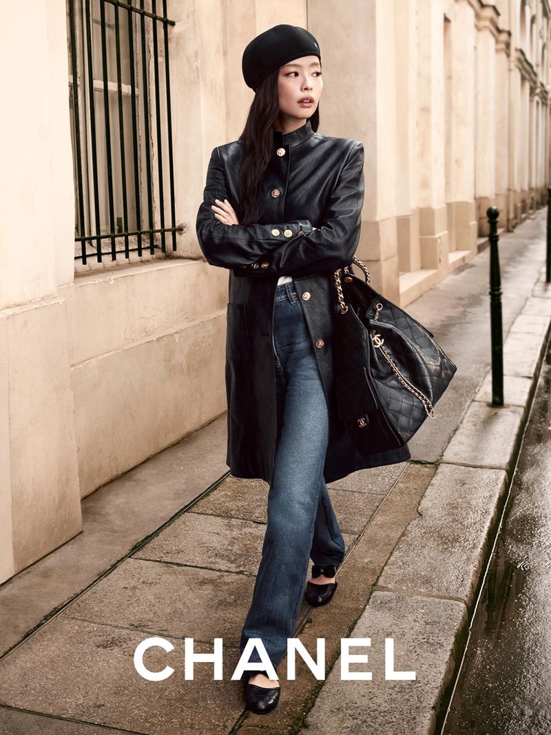 Elegant woman in a black leather coat and beret walks on a city street with a black quilted purse in a fashion editorial shot.