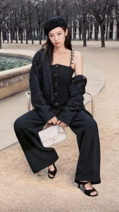 Jennie seated outdoors wearing a black beret, tweed jacket, and trousers, holding a white quilted handbag.