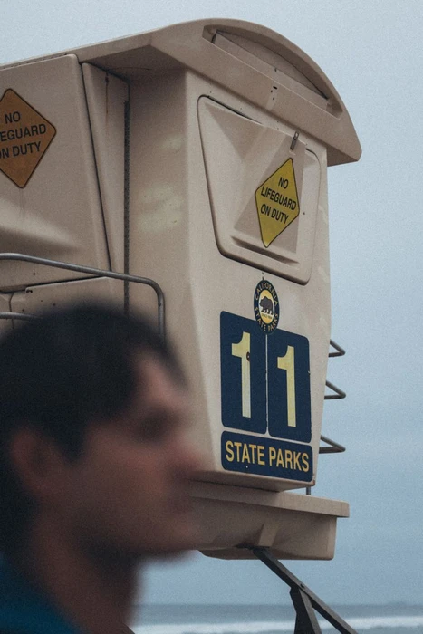 Close-up of a beige California State Parks lifeguard tower numbered 11 with a person blurred in the foreground.