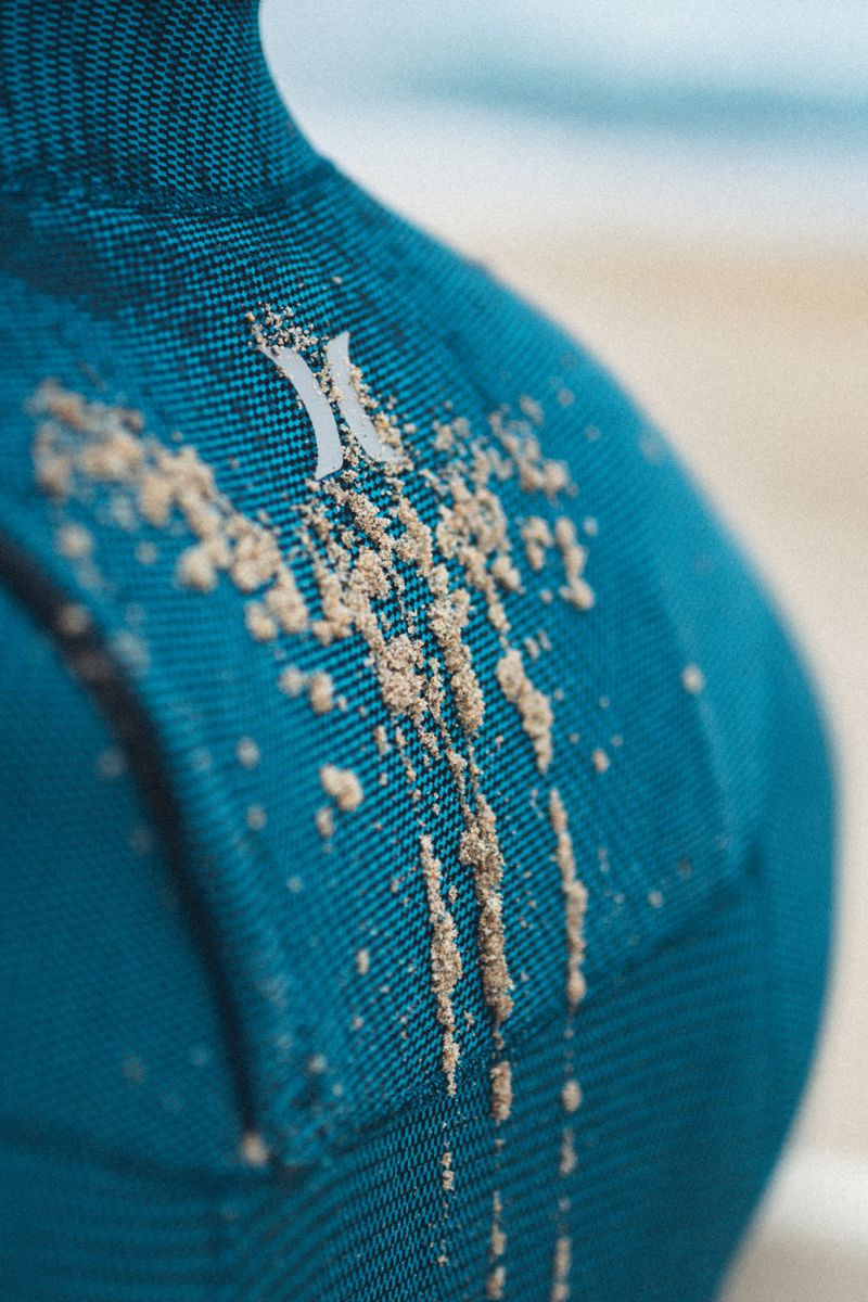 Close-up of a teal wetsuit shoulder covered in fine sand grains, photographed for MORNING MIST by MMScene.