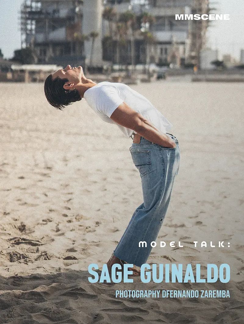 Man wearing a white t-shirt and blue jeans leaning backward on a sandy beach