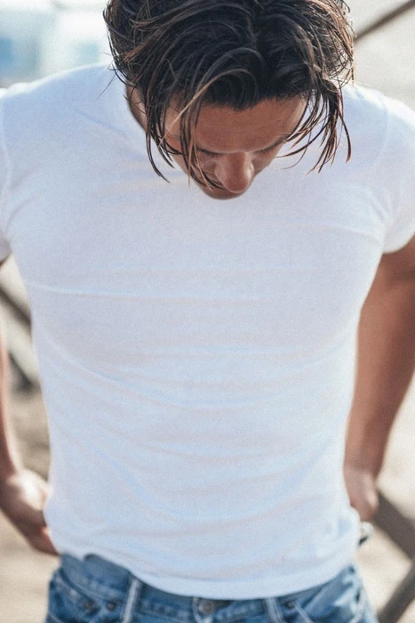 Close-up portrait of a man wearing a white t-shirt and blue jeans, looking down.