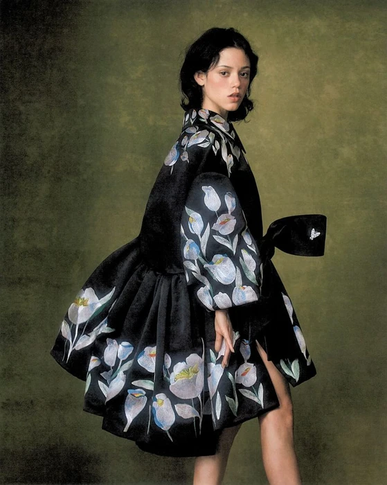 Jenna Ortega wearing a black dress with floral embroidery and puff sleeves against a textured olive green backdrop.