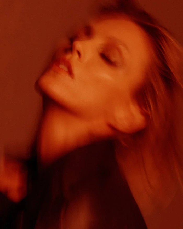 Model Anja Rubik with head tilted back in warm red lighting for Double Vision by Luigi and Iango