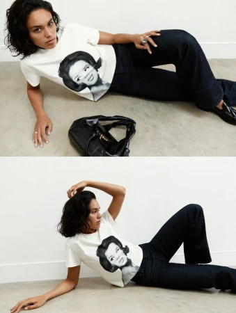 Model Anne Spoel reclining on a studio floor wearing a white graphic t-shirt, dark denim jeans, and black loafers.