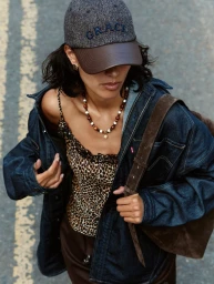 Model wearing a denim jacket, leopard print top, and tweed baseball cap standing outdoors on a paved street.