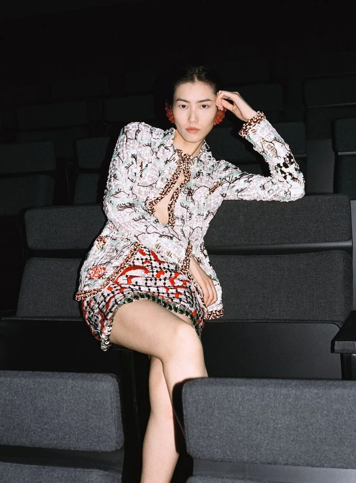 Model Liu Wen seated in a dark auditorium wearing a patterned jacket and skirt for Wallpaper China.