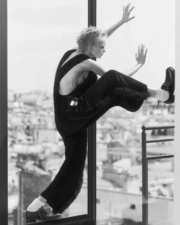 Model Gretchen Easterwood in black textured overalls and leather shoes posing dynamically against a high-rise city window.