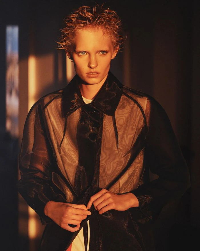 Model with short spiky hair in a sheer dark jacket under warm golden lighting for Re-Edition Magazine