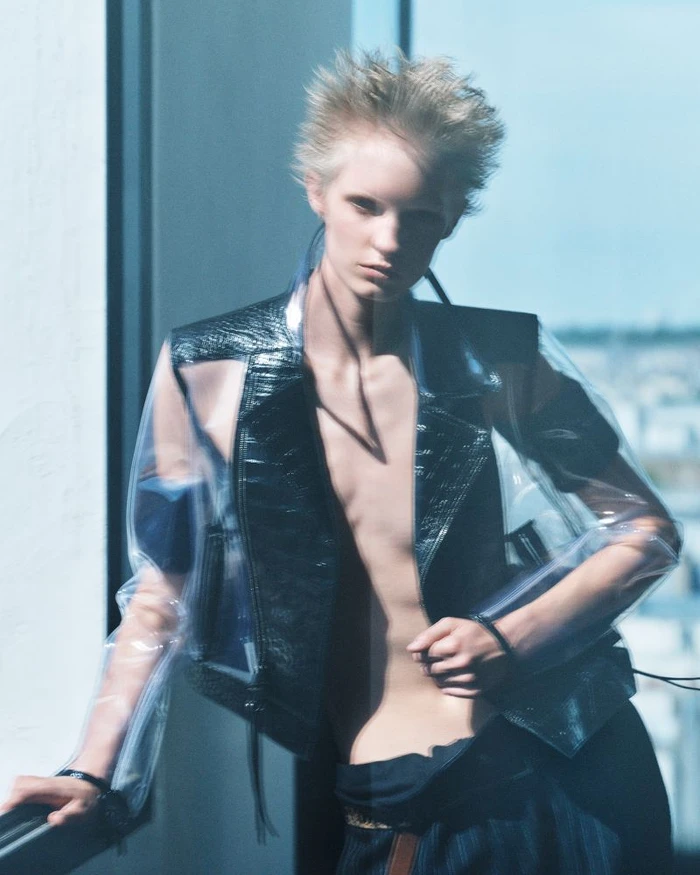 Model with spiky blonde hair wearing a transparent plastic jacket over a black vest for Re-Edition Magazine photographed by Ilya Lipkin.