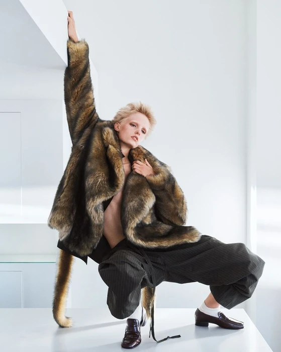 Model Gretchen Easterwood wearing a fuzzy faux fur coat and dark trousers posing in a bright interior for Re-Edition