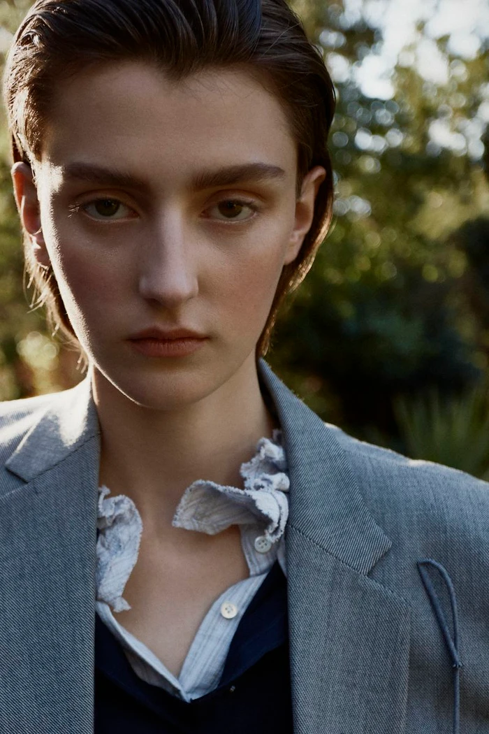 Portrait of a model with slicked-back hair wearing a grey blazer outdoors