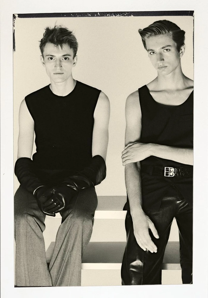 Two male models in black tank tops sitting against a light background for Le Mile Magazine editorial