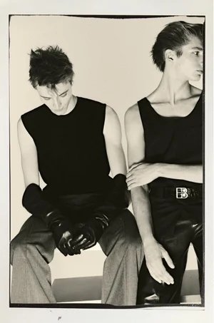 Two male models in black sleeveless tops and trousers sitting against a plain light background for Le Mile Magazine.