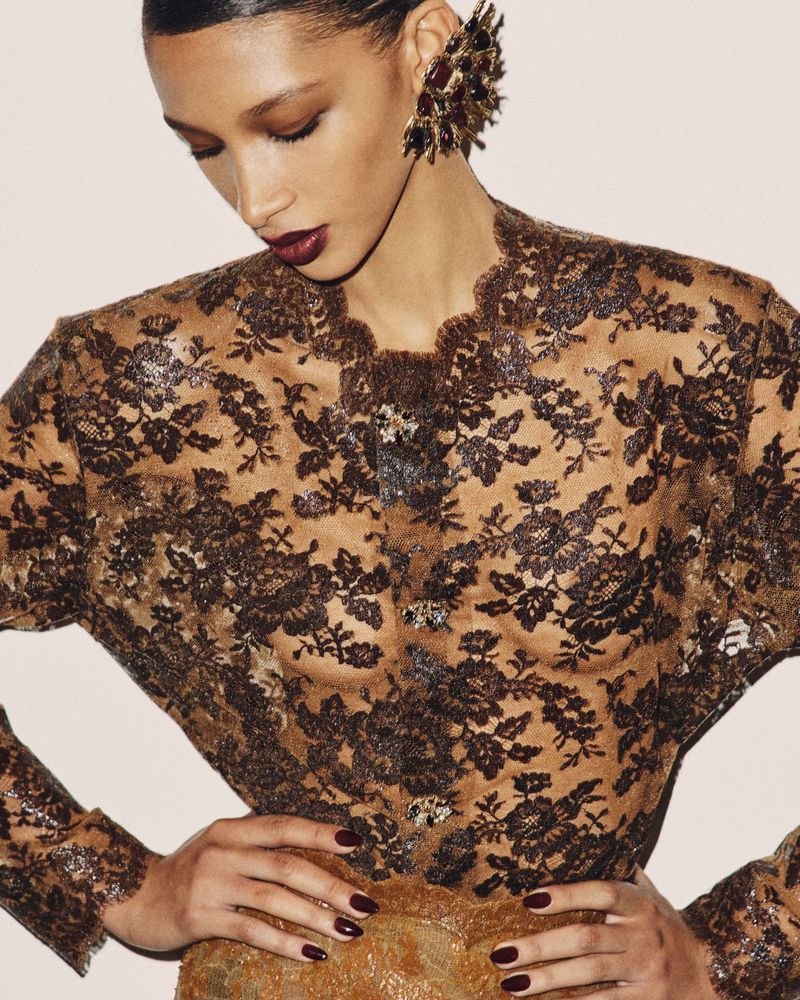Model wearing a sheer brown lace top and ornate jewelled ear cuff against a plain light background
