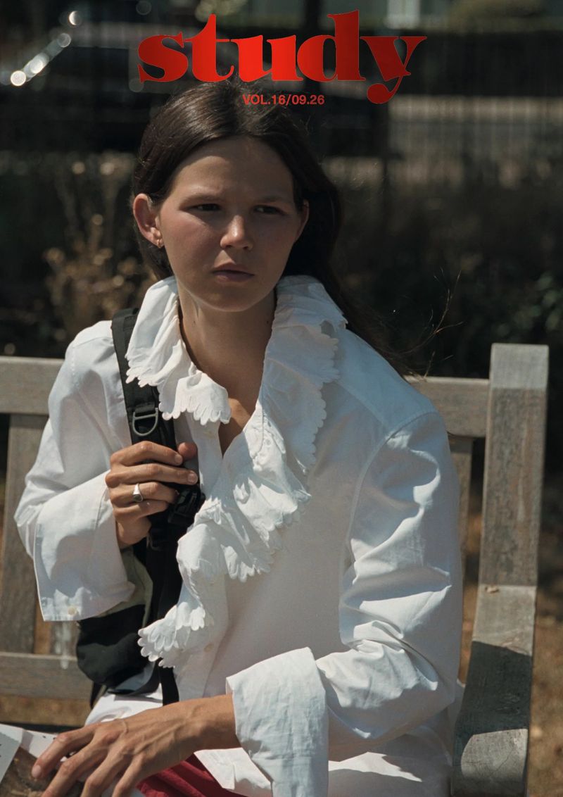 Model wearing a ruffled white shirt seated on a wooden bench outdoors for Study Magazine Vol.16 09.26.