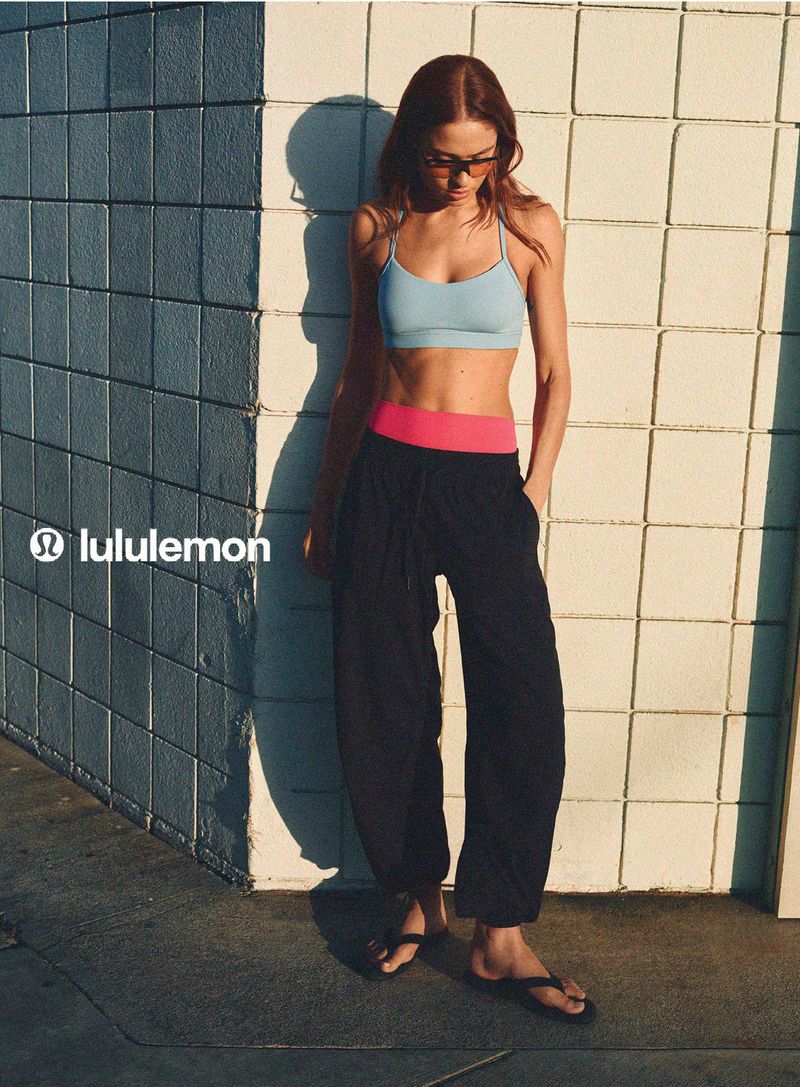 Model in blue sports bra and black trousers standing against a tiled wall outdoors in bright sunlight for lululemon