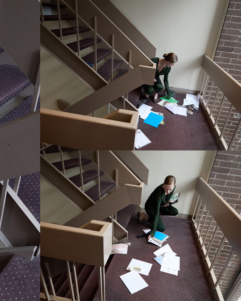 Woman in a green jumpsuit crouches on a staircase with scattered papers, looking down at the papers.