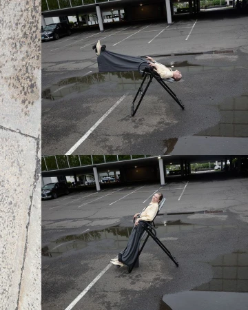 Man rests on an inversion table in a parking lot with puddles, showcasing a humorous juxtaposition of leisure and an urban environment.