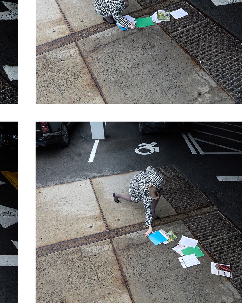 High-angle shot of a person picking up papers in a parking lot, wearing a houndstooth coat with a car visible in the background.