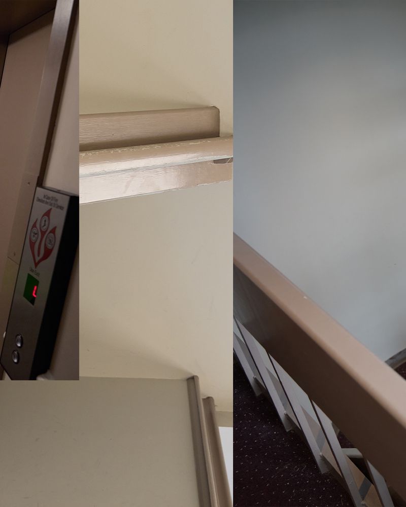 Interior view showing an elevator control panel with lit floor number, adjacent wall, and railing with stairs in the background.