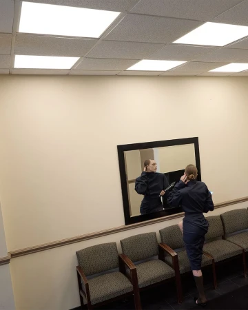 An adult female in dark business attire adjusting her hair, as reflected in a mirror, in a commercial interior setting with row seating.