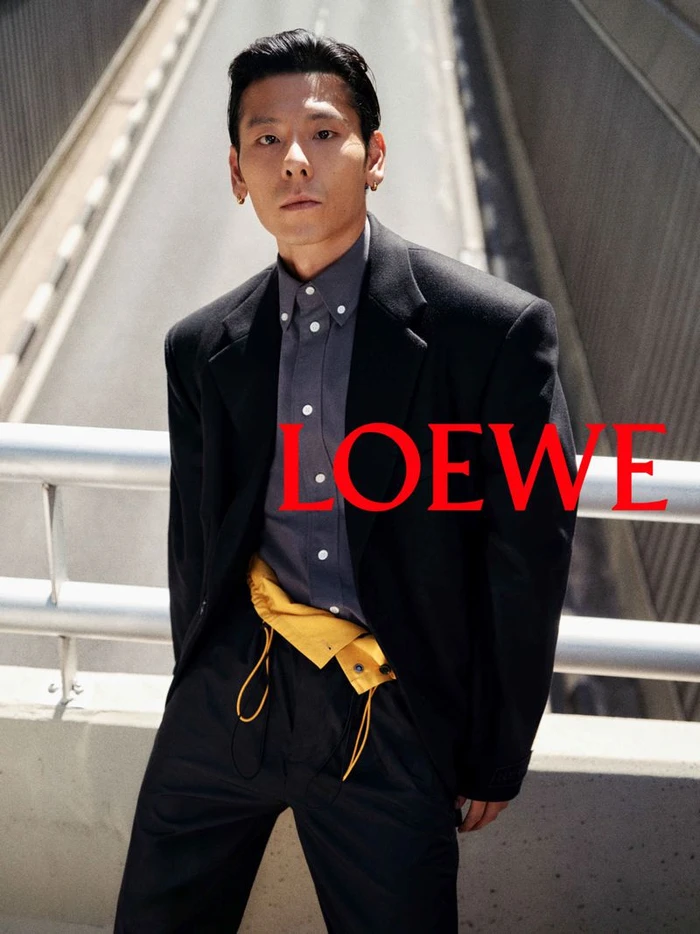 Man wearing a black blazer and grey shirt posing against a bridge railing for Loewe pre collection campaign
