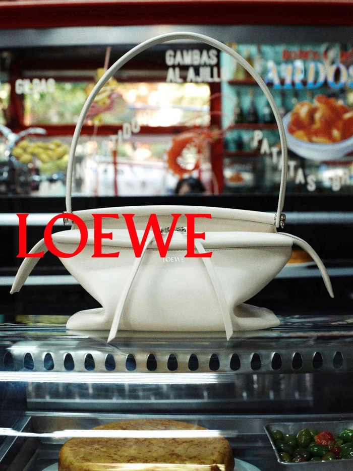 Off-white leather handbag on a glass display counter with red Loewe typography overlay