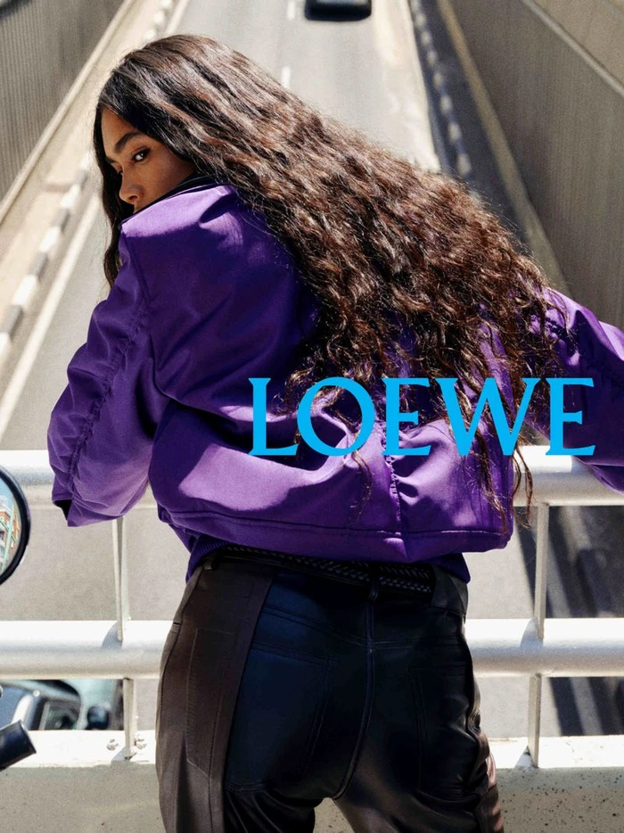 Model in a purple jacket looking back while leaning against a bridge railing over a road
