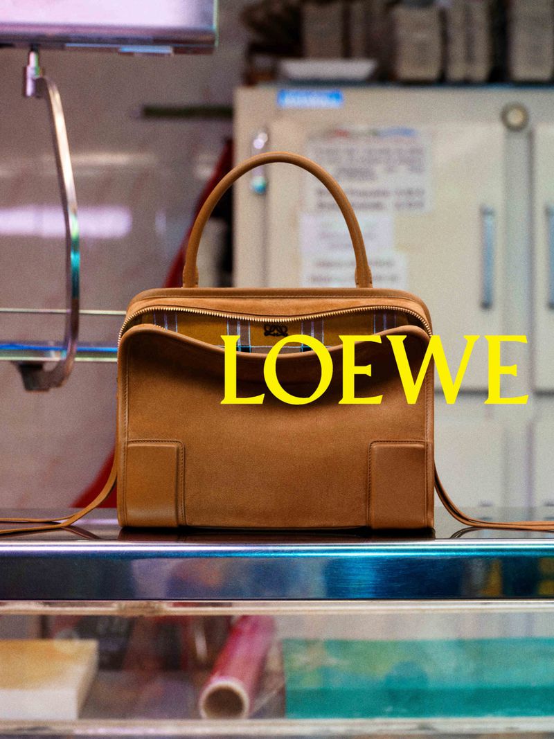 Brown leather handbag centered on a reflective glass shelf with bright yellow text overlaid reading Loewe
